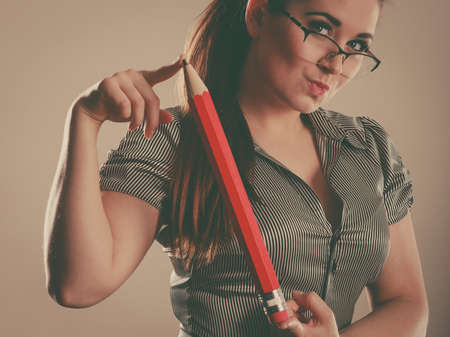 Teacher looking elegant woman wearing grey shirt and eyeglasses holding big oversized pencilの写真素材