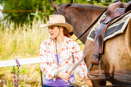 Taking care of animals, horsemanship, equine concept. Cowgirl getting horse ready for ride on countryside.の写真素材