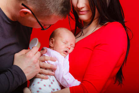 Family, childhood and parenthood concept. Little newborn baby sleeping on mother chest, dad brushing child hair . Red backgroundの写真素材