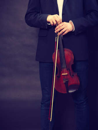 Music passion, hobby concept. Man man dressed elegantly holding wooden violin. Studio shot on dark...