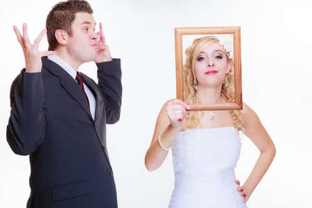 Wedding day, negative relationship concept. Groom and bride holding, posing with empty photo frame having bad argument.の写真素材