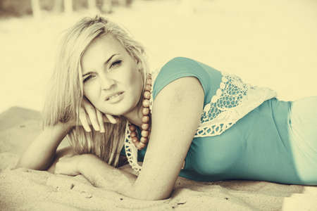 Holidays relax time concept. Blonde woman lying on sand. Lady has big necklace. Female is chilling on the beach.の写真素材