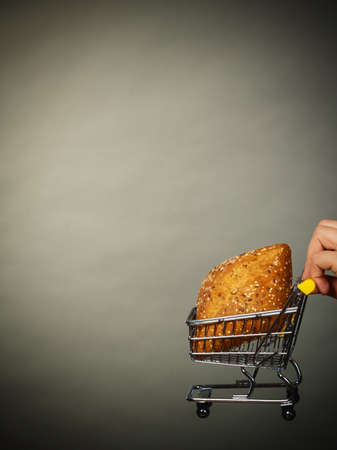 Buying gluten food products concept. Woman hand holding shopping cart trolley with small piece of breadの写真素材