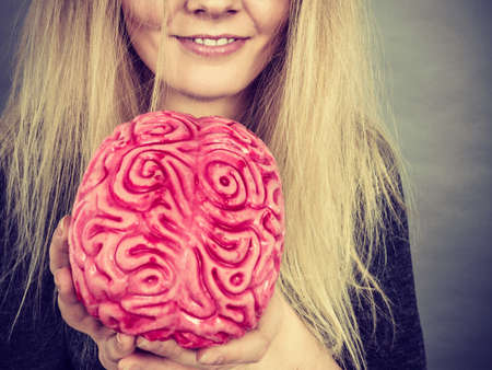 Weird blonde woman holding brain having something on mind, thinking of idea.の写真素材