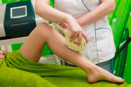 Medical cosmetology, modern cosmetic devices concept. Woman lying on back, getting laser treatment on her legs in beauticianの写真素材