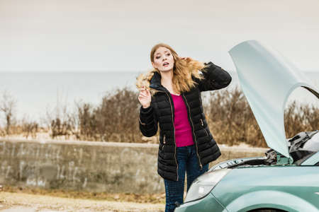 Accident and breakdowns with auto concept. Blonde woman and broken down car on road checking problem in engineの写真素材
