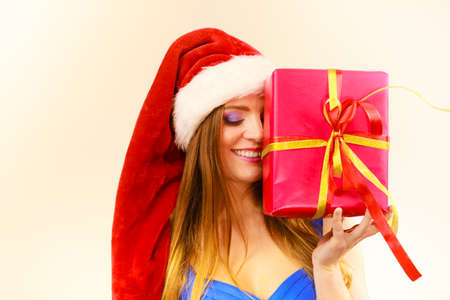 Lovely woman wearing santa claus hat holding big red christmas present, hiding her face behind gift....