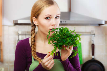 Woman in kitchen holding green fresh aromatic parsley leaves. Young housewife cooking. Healthy eating, vegetarian food, dieting and people concept.の写真素材