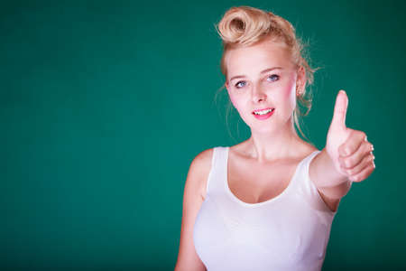 Symbols, gestures concept. Smiling young woman with pinup hair making thumb up gesture. Studio shot on green backgroundの写真素材