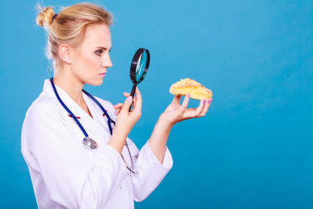 Dietitian nutritionist checking examine sweet roll bun with magnifying glass. Woman with fattening junk food. Bad unhealthy eating nutrition concept.の写真素材