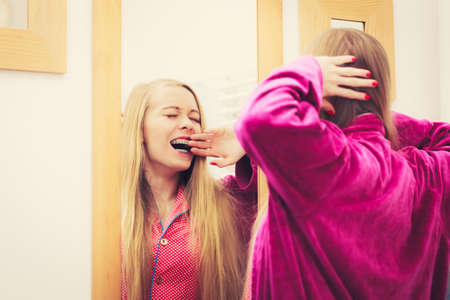 Sleepy awaken woman standing in bathroom looking at her reflection in mirror after morning getting up yawning and stretchingの写真素材