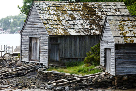 Beautiful landscape view of old norwegian cottage by lake coast and forest, water mirror reflecting on sunny day.の写真素材