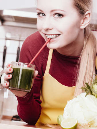 Drinks good for health, diet breakfast concept. Young woman in kitchen holding green healthy vegetable smoothie juice glassの写真素材
