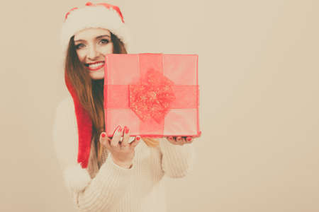 Gorgeous woman wearing santa claus hat holding red big gift box with ribbon. Xmas, happiness, winter and people concept.の写真素材