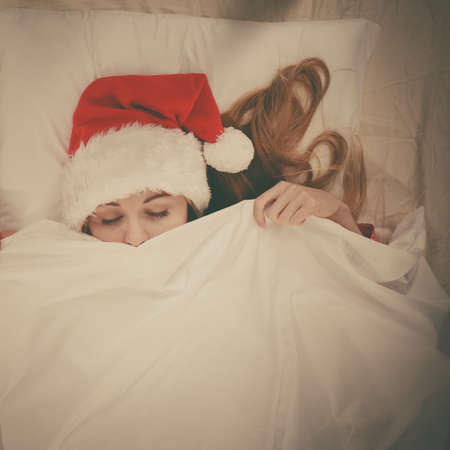 Woman waiting for Christmas season wearing pajamas and Santa Claus hat lying in bed.の写真素材