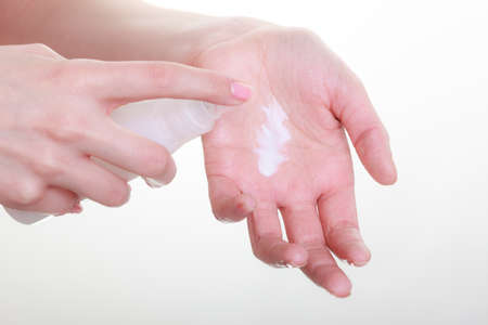 Beauty, cosmetics, concept. Woman applying white moisturizing cream from bottle with pump on hand to test product. Studio shot on white backgroundの写真素材