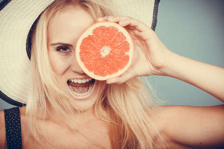 Healthy diet, refreshing food full of vitamins. Woman wearing sun hat holding sweet delicious red grapefruit fruitの写真素材