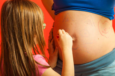 Childhood, family love concept. Toddler girl drawing on her mother big pregnant belly