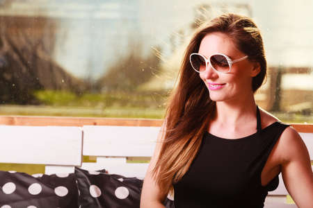 Relaxation concept. Young woman wearing black dress bright jacket sitting on bench. Fashionable female model resting spending free time.の写真素材