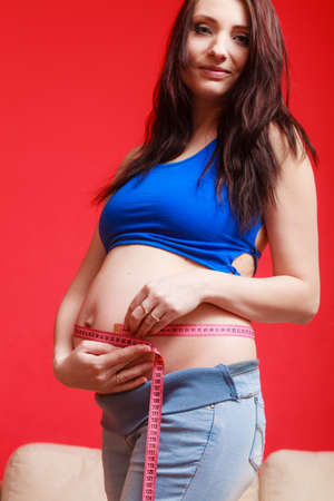 Pregnancy, parenthood concept. Pregnant woman measuring her belly with tape.の写真素材