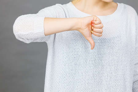 Unlike, dislike, failure gestures concept. Woman showing thumb down gesture, studio shot grey background.の写真素材