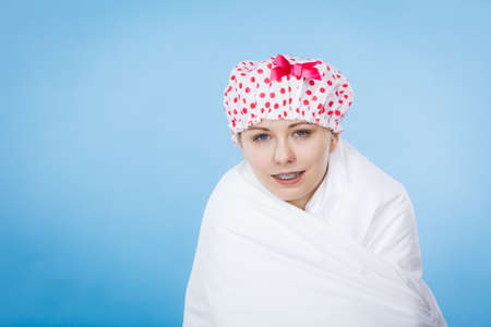 Funny happy woman after shower wearing pink pajamas and dotted bathing cap sitting on bed covered with white fresh blanket.の写真素材