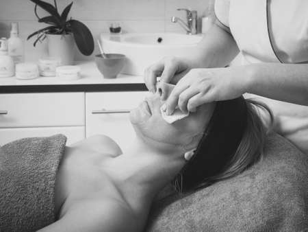 Beautician wiping off green algae mud mask on woman face in salon. Beauty, relaxation, skincare, wellness in spa concept. Black and white photoの写真素材