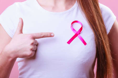 Healthcare, medicine and breast cancer awareness concept - Closeup of pink badge ribbon on woman chest to support breast cancer causeの写真素材