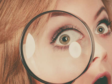Blonde woman holding magnifying glass investigating something and looking closely, trying to find solution.の写真素材
