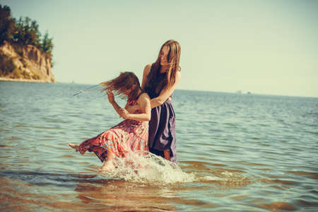 Mother and daughter having fun and playing in water near seasideの写真素材
