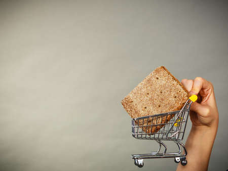 Buying gluten food products concept. Woman hand holding shopping cart trolley with small piece of breadの写真素材