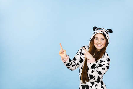 Happy teenage girl in funny nightclothes, pajamas cartoon style pointing up with positive smiling face expression, studio shot on blue. Advertisement conceptの写真素材