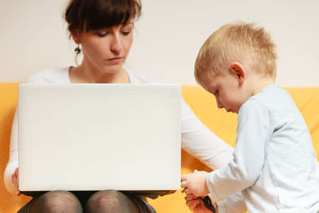 Working at home problems concept. Mother working and using laptop her little boy disturbing