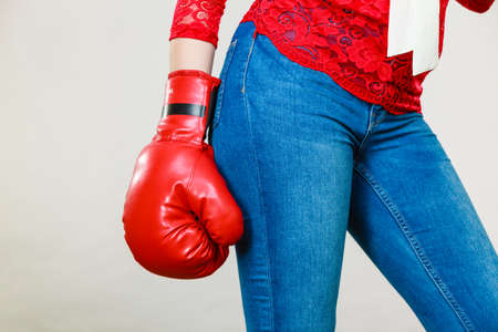 Unrecognizable woman wearing red boxing glove, and tight blue jeans. Grey background.