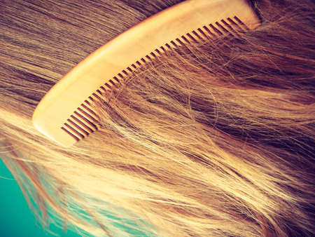 Haircare concept. Straight brown hair with wooden comb closeup