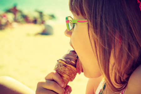 Toddler girl eating ice cream on beach near sea