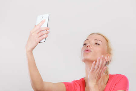 Technology, modern photography, confidence conept. Happy attractive adult blonde woman taking picture of herself with smartphone, selfie.の写真素材
