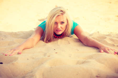 Portrait of attractive blonde woman lying on sandy beach relaxing during summertimeの写真素材