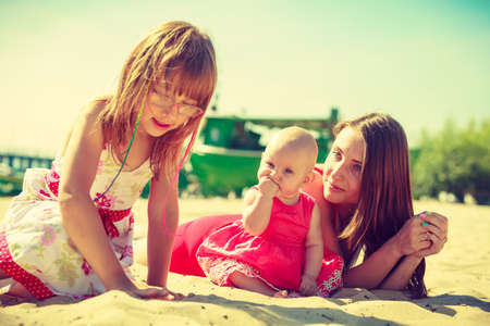 Mother, baby and toddler girl in summeral clothing playing on beach near seaの写真素材
