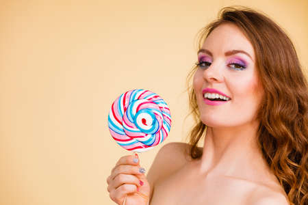 Beautiful woman bare shoulders holding big lollipop candy in hand, closeup. Sweet food and fun concept. Studio shot on brightの写真素材