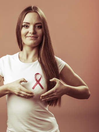 Awareness of breast cancer.Young woman making heart shape by hands on pink ribbon symbol sign. Help and charity. Gray backgroundの写真素材