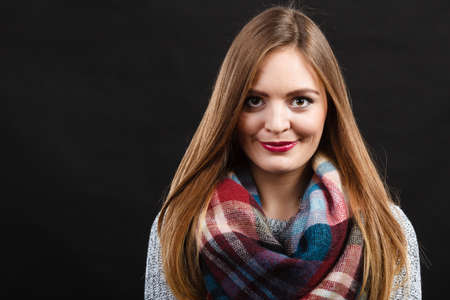 Autumnal outfit concept. Smiling female long hair wearing warm autumn clothing plaid woolen scarf, on darkの写真素材