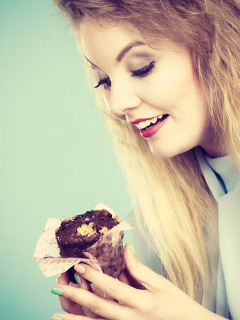 Sweet food sugar make us happy. Attractive blonde woman holds yummy chocolate cupcake in hand, craving for cake. Appetite and tasty meal dessert.の写真素材