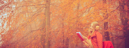 Outdoor nature season relax leisure concept. Young lady with literature. Blonde girl reading red...