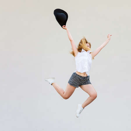 Vacation and happiness concept. Blonde woman wearing summer clothes jumping with sun hat in hand