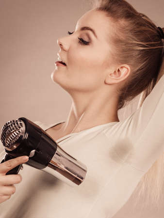 Woman drying wet armpit using hair dryer. Getting rid of sweat and bad smell, hyperhidrosis.の写真素材