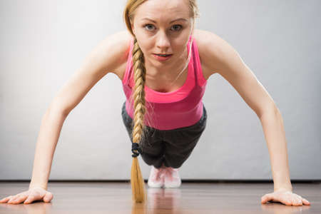 Young woman wearing sportswear doing push ups. Training at home, being fit and healthy.
