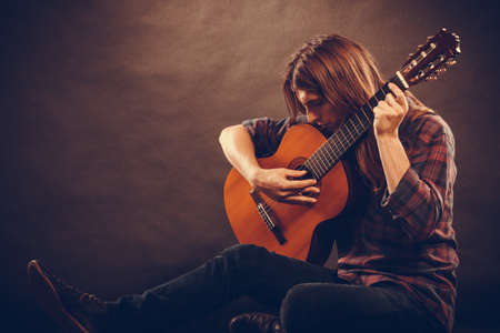 Hobby, music concept. Artist with his wooden guitar. Young man is sitting on the ground holding the...