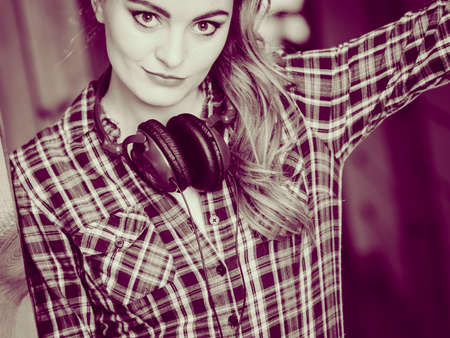Hobby music style and free time. Young girl with headphones stand indoor wear fashionable clothes.