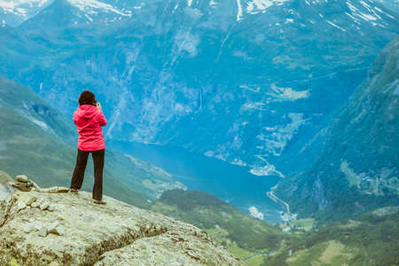 Tourism vacation and travel. Female tourist taking photo with camera, enjoying Geiranger fjord and...